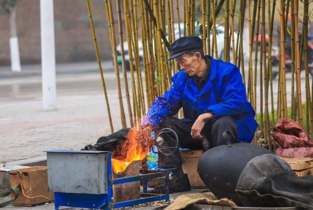 他坐在一个小木箱上,熟练地舀起玉米粒装进老式爆米花机中,拧紧盖子