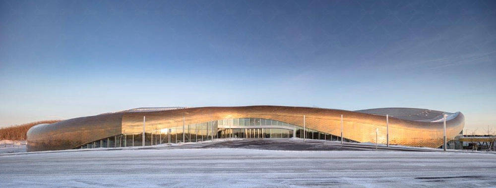 这座起伏的蛇形建筑拥有巨大的占地面积,有着闪闪发亮的黄铜带状外墙