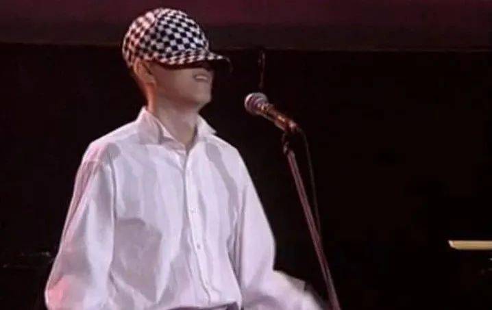 个带着黑白格子帽子的男孩叫上前来唱歌,这个男孩就是年轻时的梁翘柏