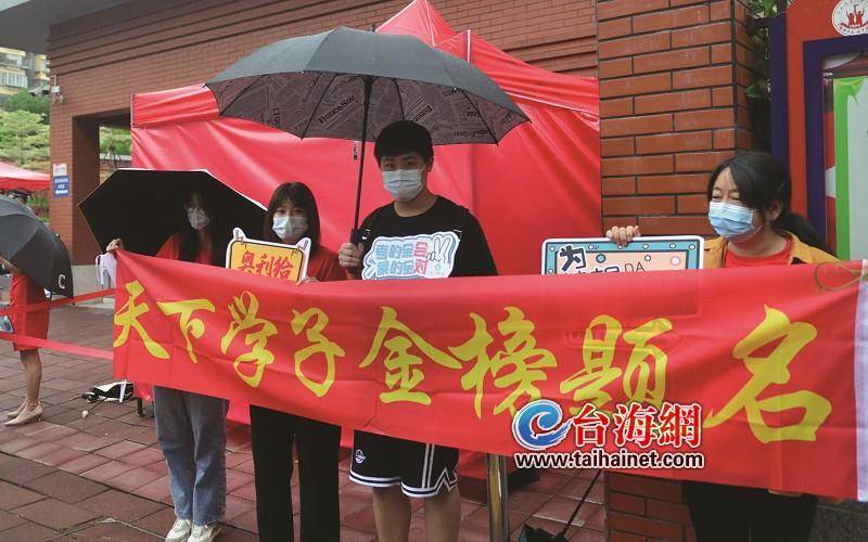 穿着红色t恤,拉着印有"天下学子金榜题名"标语的横幅,手里拿着"为梦想