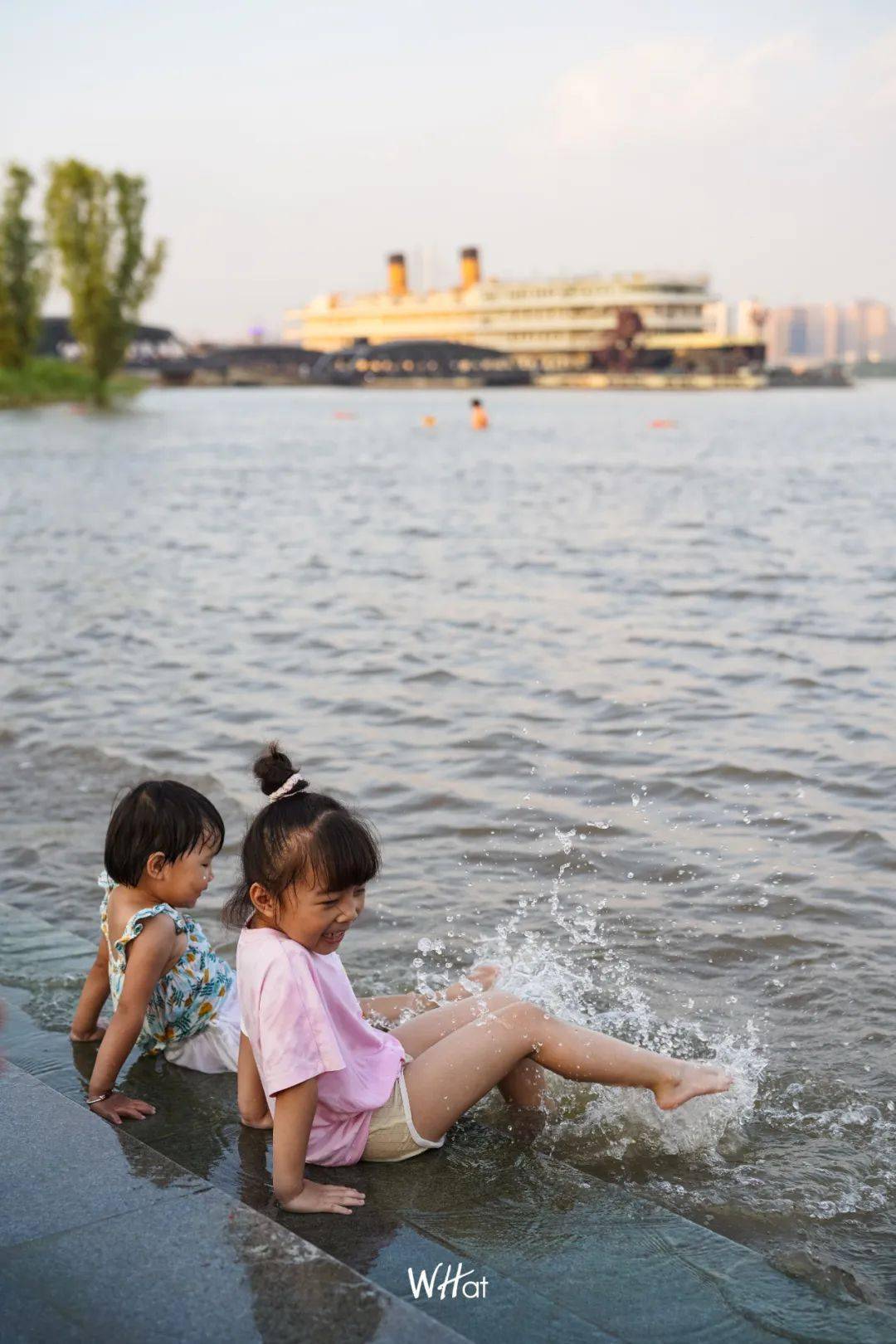 小女孩坐在江水里的瓷砖上,用脚击打出成片的浪花;大人们坐在岸边